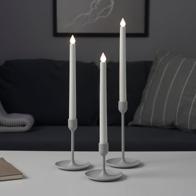 Three modern silver candlesticks in varying heights on a table, providing atmospheric light.