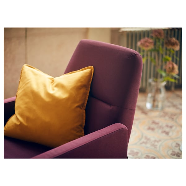 A deep purple recliner chair with a golden pillow, positioned in a cozy room with a patterned rug.