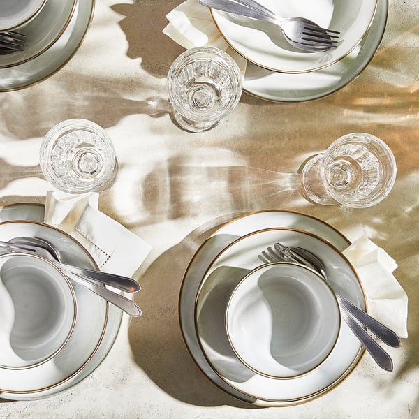 Four place settings, each with white plates, silverware, glasses, and folded napkins. Elegant and classic table decor.