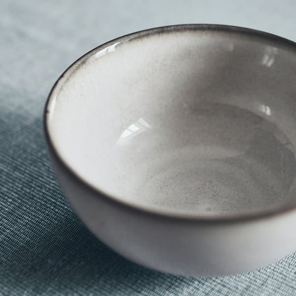 Smooth-edged glazed bowl, gray inside, on green fabric.