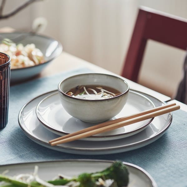 Small bowl of soup with chopsticks on plates, served on a blue tablecloth.