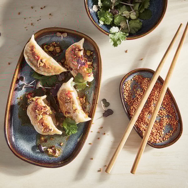 Blue stoneware plate with dumplings and chopsticks.