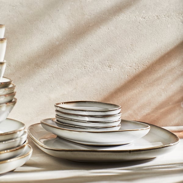 A stack of light gray, stoneware plates with a textured glaze and slightly irregular shape, arranged neatly for a table setting.