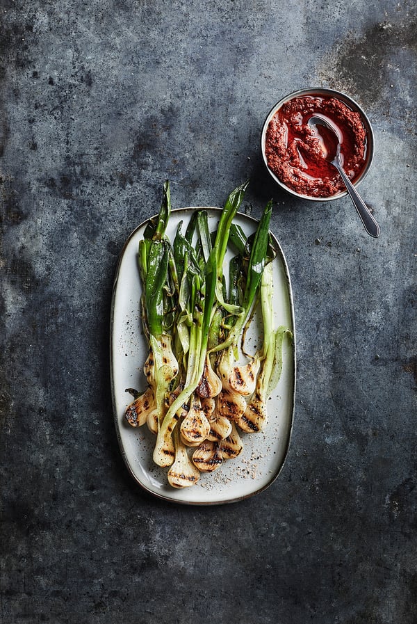 A white oval platter with grilled green onions and mushrooms, accompanied by a small bowl of red sauce.