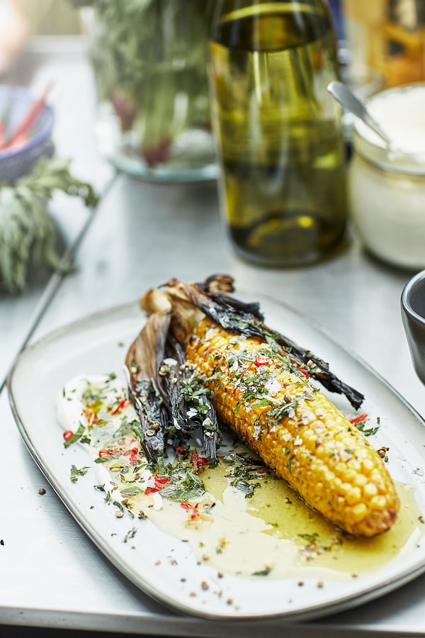 GLADELIG sand-colored stoneware plate featuring grilled corn, garnished with herbs and spices. Elegant, rustic design.