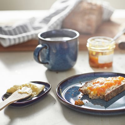 Blue glazed plate with toast & jam, mug, and honey, sunlit.
