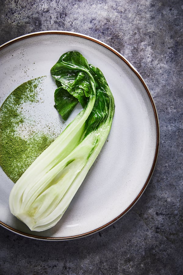 GLADELIG white plate with green leafy vegetable, light glaze, stoneware, round shape, minimal design.
