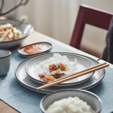 Table setting with GLADELIG side plate, chopsticks, and small bowls, featuring reactive-glaze design, ready for meal.