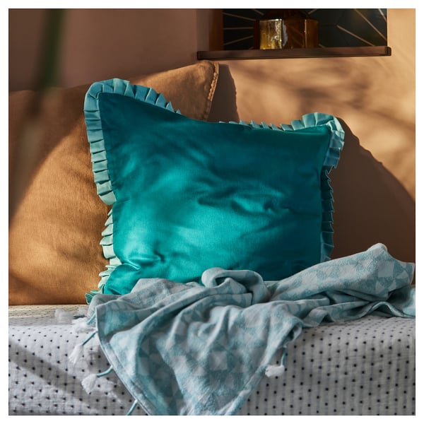 Bright blue satin-like pillow with ruffles on a brown couch next to a crumpled light blue blanket.