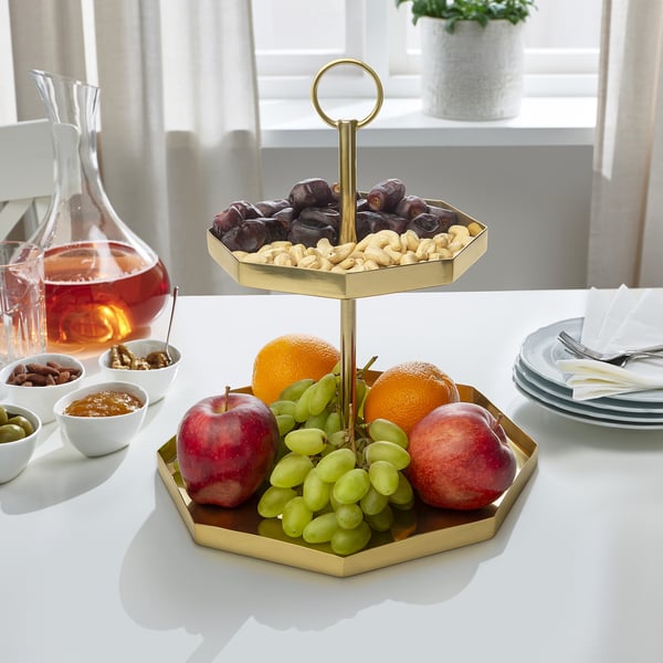 Gold-colored serving stand with two octagonal tiers holds fruit on bottom and dried snacks on top. Centerpiece for snacks and desserts.