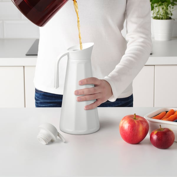 Person pouring liquid into insulated flask on counter with fruits.