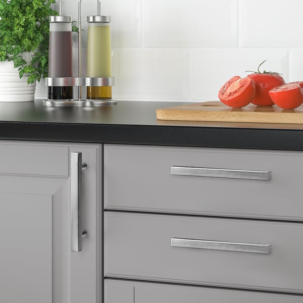 Modern kitchen with grey cabinets, silver GRIBBOL handles, black countertop. Small tomatoes, herbs, and seasoning bottles on the counter.