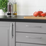 Modern kitchen with grey cabinets, silver GRIBBOL handles, black countertop. Small tomatoes, herbs, and seasoning bottles on the counter.