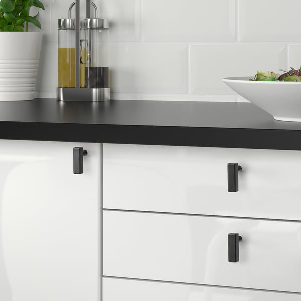 Modern kitchen with black GRIBBOL knobs, metallic drawer handles, salad bowl, oil dispensers on dark countertop.