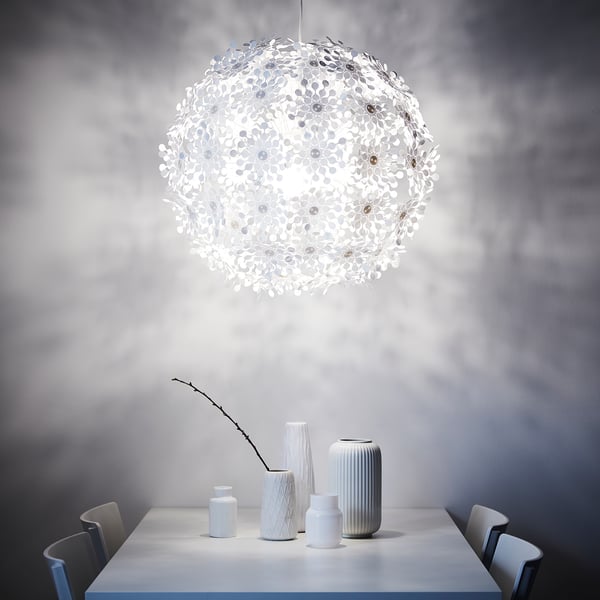 Modern dining setup with white hanging lamp emitting soft glow, surrounded by various white vases on table.