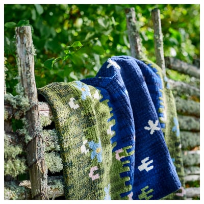 Hand-woven GRODDSVINGEL rug with green, blue, and white floral design on a navy center. Wool and cotton material, rectangular shape.