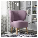 Purple GUBBO armchair with wooden legs next to shelves and a lamp.