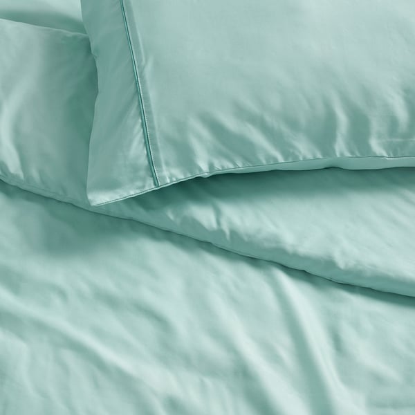 Close-up of a luxurious turquoise duvet cover and pillowcases, showcasing smooth, elegant piping and high-quality fabric.