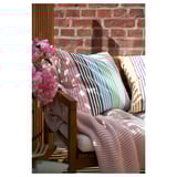 Colorful striped outdoor cushions on wooden bench with pink flowers and brick wall.