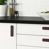 Kitchen counter with black countertop, featuring white cabinets with modern purple handles, a bowl of salad, and oil dispensers.