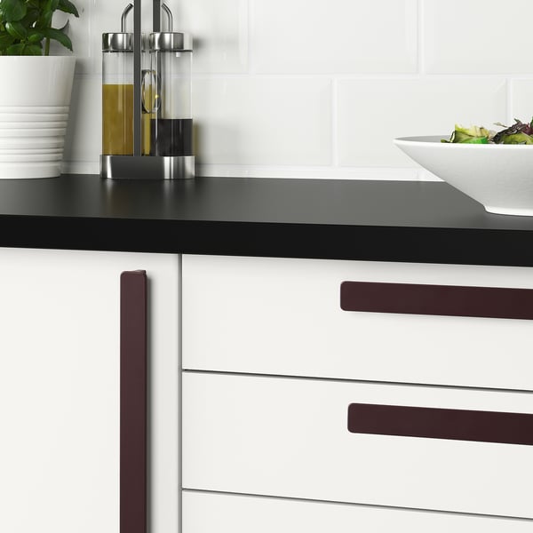 Modern kitchen with white drawers and a black countertop. Dark handles on drawers, and oil dispensers and a green salad bowl on the counter.