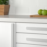 Kitchen with modern white cabinets. Limes on wooden board, plant in basket, gray tile backsplash. Handle labeled ikea.