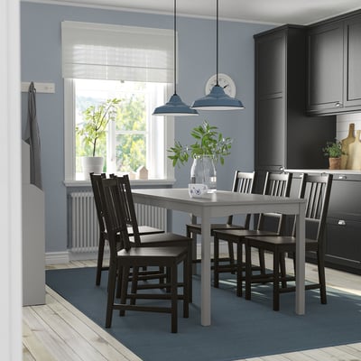 Modern kitchen with HAUGA table, dark chairs, blue lights. Black cabinets, large window. Grey rug.
