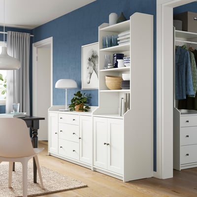 Modern room with blue walls, white HAUGA unit, vases, books, lamp, plant, open & closed storage.