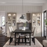 Modern dining room with black HAVSTA table, cream chairs, and striped wallpaper, featuring glass-fronted cabinets displaying whites and greens.