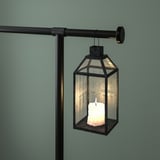 A hanging lantern with a lit candle inside, suspended from a decorative rod clamped to a table.