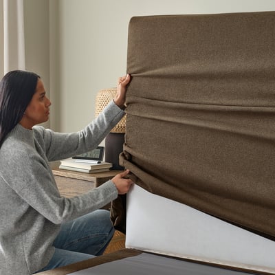 Woman adjusting HEMFJÄLLET divan bed cover, showing removable and washable feature.