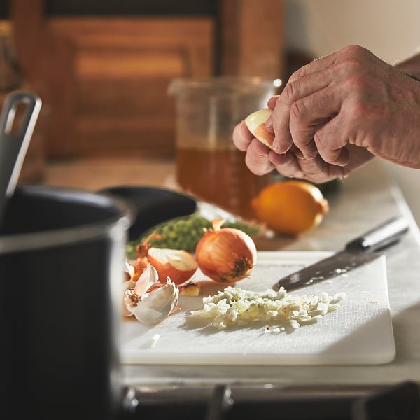 Person squeezing lemon over garlic, onions, and veggies on white cutting board in kitchen.