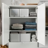 White cabinet with folded clothes, organized in sections, top shelf has a glass vase and stacked books.