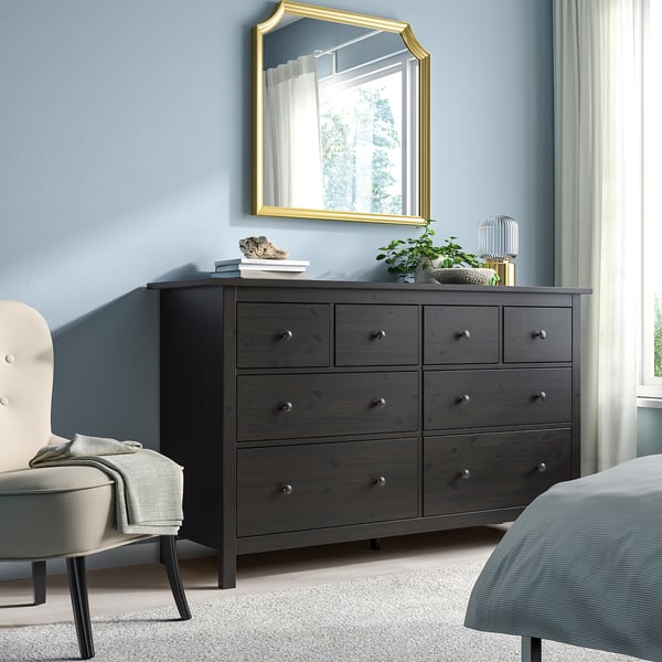 Bedroom with wide HEMNES dark wood dresser, mirror, white chair, & bed against blue wall.