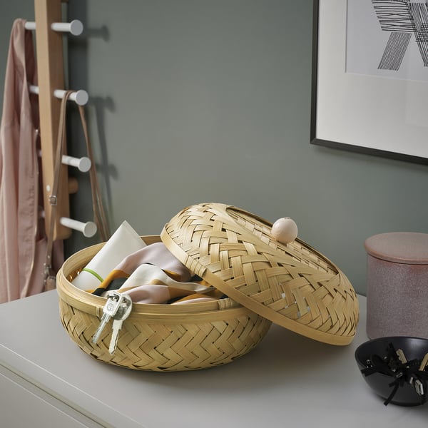 Woven bamboo storage basket with lid, holding keys and small items, on a white surface.