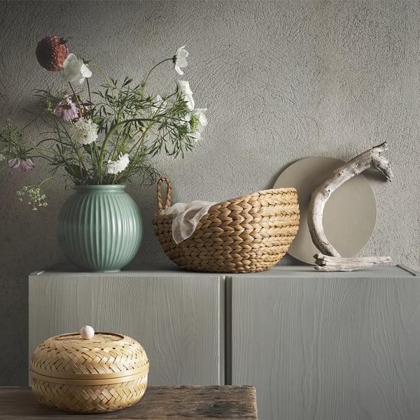 Styled natural scene: green vase, woven baskets, driftwood circle on grey shelf.