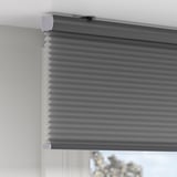 A window with a rolled-down gray cellular blind, offering room-darkening and privacy. The blind has a hidden cord for safety.