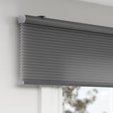 Gray room-darkening cellular blind with hidden cord, mounted on wall, providing privacy and insulation.