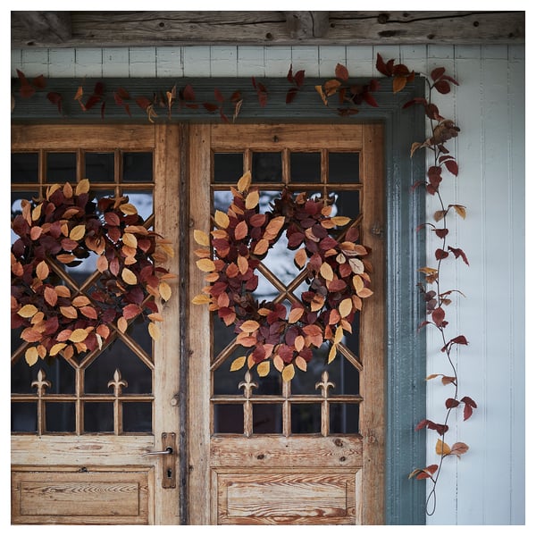 HÖSTAGILLE wreaths decorate rustic doors. Large, autumnal wreaths of reds & golds hang prominently on double doors adorned with dried leaves.