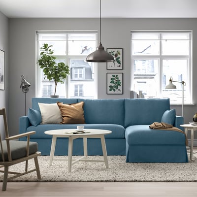 Modern living room with blue sectional, grey rug, white table, lamp, art, and large windows.
