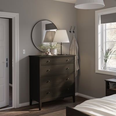Cozy bedroom with IDANÄS dark brown dresser, mirror, lamp, and hooks; white bedding and window.