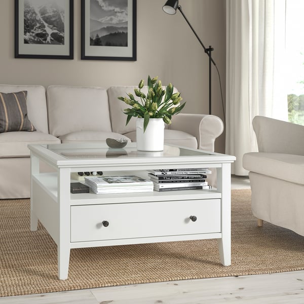 IDANÄS coffee table with glass top & drawer in living room, flanked by sofas, holding vase, books, and bowl.