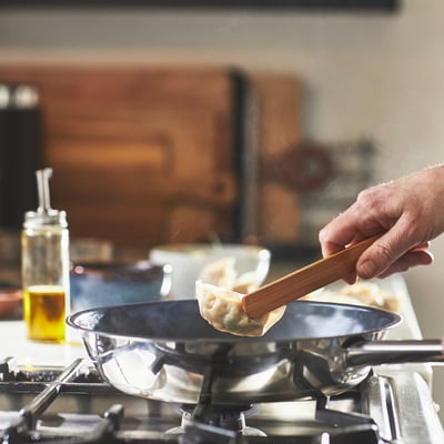 Hand flips dumpling in non-stick pan on gas stove.
