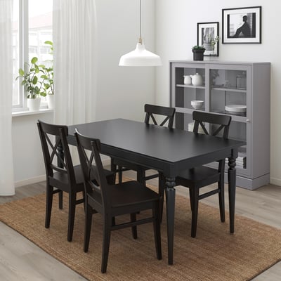 Black extendable dining table with 4 chairs, large rug, grey bookshelf.