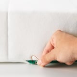 Hand using a paper clip to open a child-safe zipper on a white mattress.