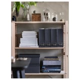 Bookshelf with wooden shelves, stacks of books, decorative glass jars, vases with greenery. Organized, stylish display.
