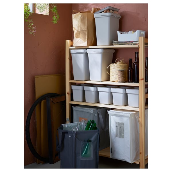 An IVAR storage unit with grey plastic bins and fabric bags on wooden shelves against a red wall.