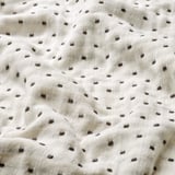Close-up of a soft, white cotton blanket with even, decorative grey stitching, highlighting its natural and durable quality.