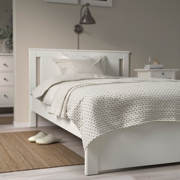 Minimalist white bedroom with off-white JAKOBSLILJA bedspread, slippers, dresser, wall lamp.