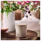White textured candle in ceramic jar beside ribbed vase with vibrant flowers on wooden table.
